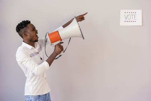 A passionate man urging people to vote using a megaphone, pointing at a sign.